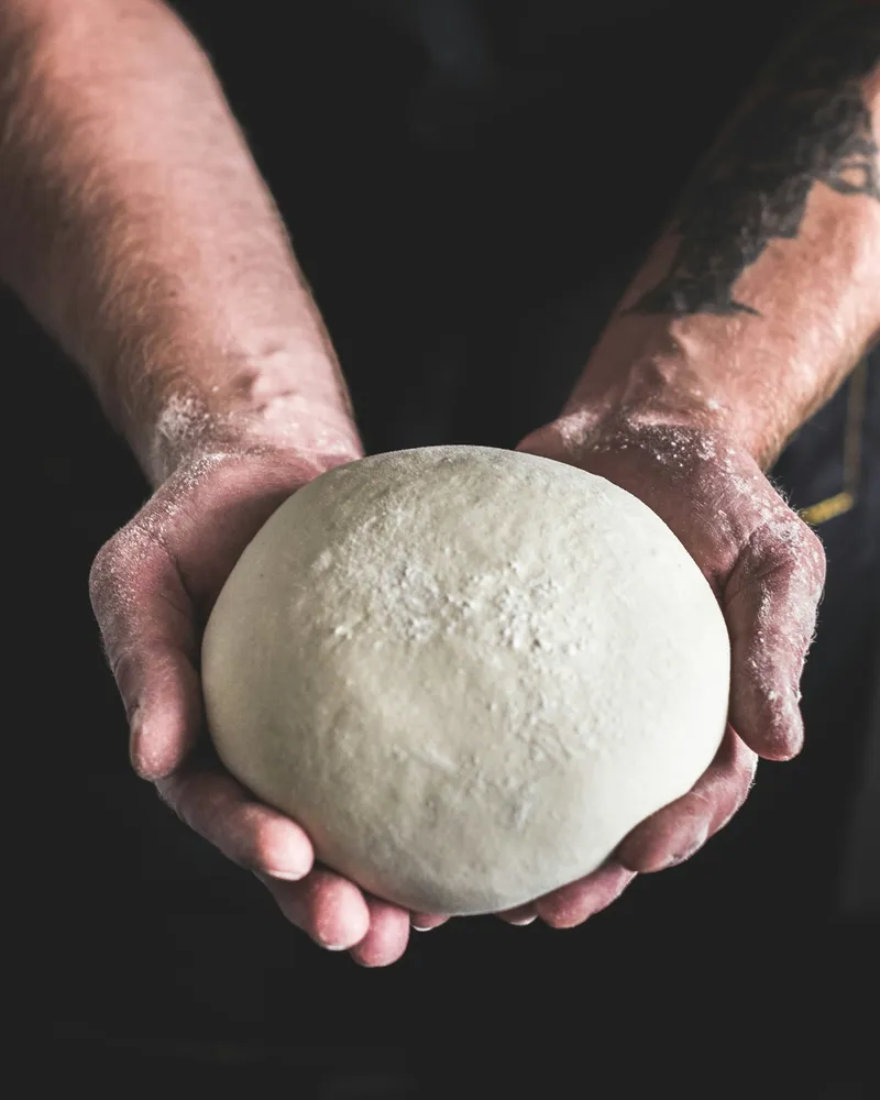 Hände formen einen Pizzateig auf bemehltem Holz