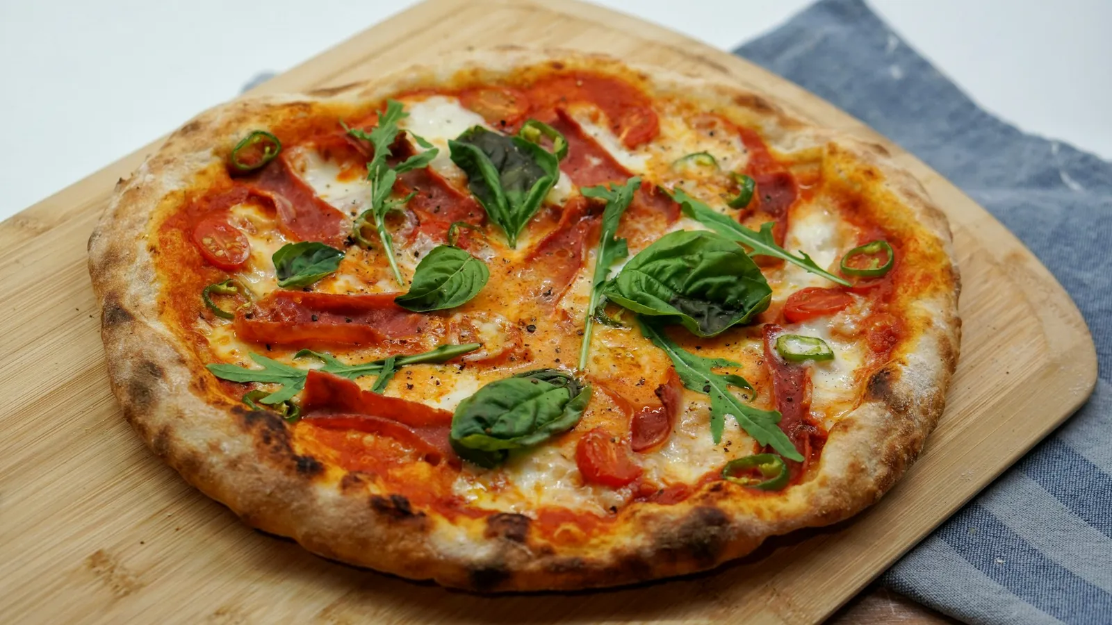 Pizza mit Salami, Cherrytomaten, Basilikum und Rucola auf einem Holzbrett