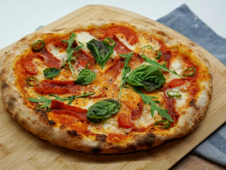 Pizza mit Salami, Cherrytomaten, Basilikum und Rucola auf einem Holzbrett