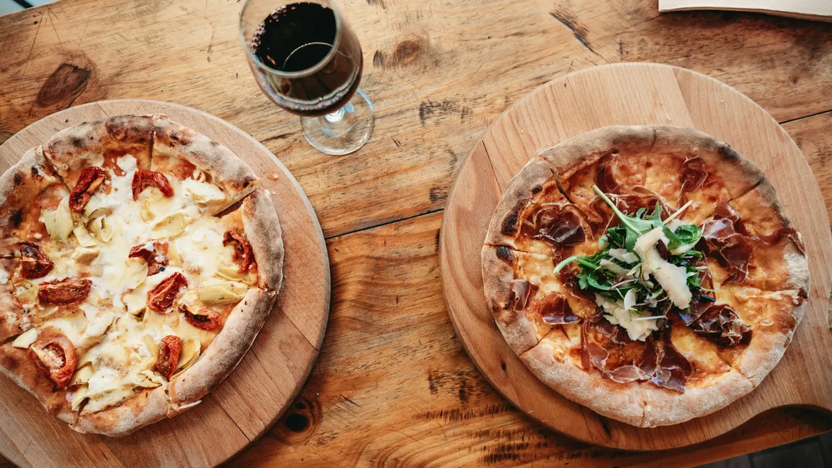 Gedeckter Holztisch mit Pizza, Pinsa und Rotwein vor dem Holzofen